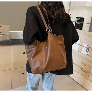 Close-up of a brown leather tote bag with a metal bar detail on a black blazer