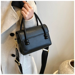 Détail du sac carré en cuir noir grainé avec bandoulière large et boucles dorées