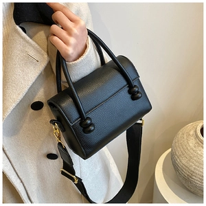 Détail du sac en cuir noir avec large bandoulière en tissu et crochets en métal doré