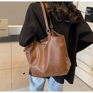 Detail shot of brown lychee-textured leather tote bag with elegant metallic bar accent