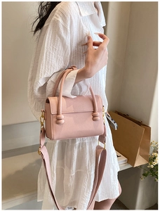 Détail d'un sac carré en cuir rose avec boucles décoratives et bandoulière large