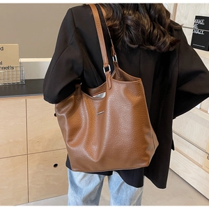 Detail of soft brown pebble leather texture and silver logo on large commuter tote bag