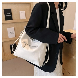 Ampia borsa a tracolla bianco crema con texture litchi indossata in una biblioteca urbana
