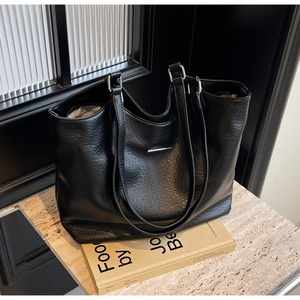 Close-up of black lychee grain leather tote bag with silver metal buckle on books
