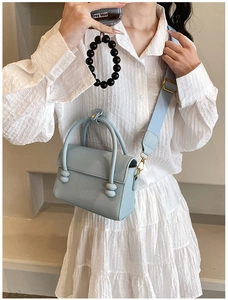 Détail du petit sac bleu clair à motif litchi avec sa large bandoulière en tissu