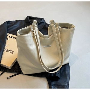 Detailed view of cream-colored tote bag with lychee texture on leather and metal bar