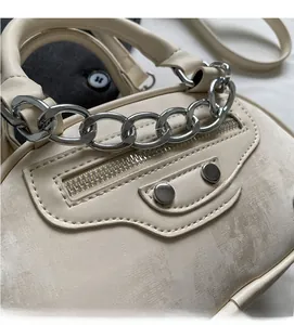 Detailed close-up of distressed cream leather texture with silver chain and metal rivets