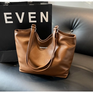 Detailed macro view of the brown tote bag's premium litchi texture and metal bar
