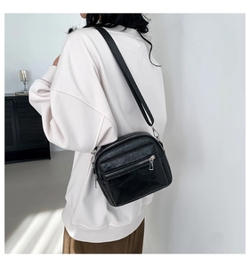 Detalle del bolso bandolera láser negro con cremalleras plateadas en el modelo