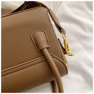 Gros plan du sac marron texturé avec surpiqûres fines et boucles en métal doré brillant