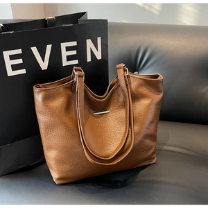 Detail of caramel brown tote bag showing pebbled leather texture and silver metal bar
