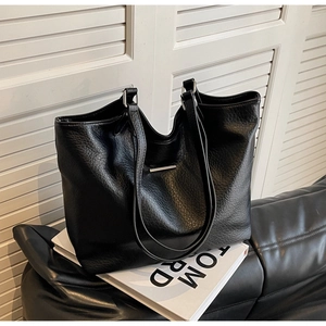 Close-up of black leather tote bag with lychee texture and minimalist metal bar detail