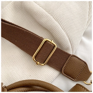Détail de la bandoulière large en toile et boucle dorée sur un sac à main en cuir
