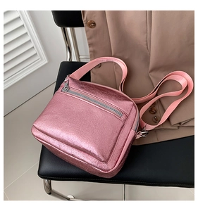 Detalle de bolso bandolera rosa metalizado con cremalleras y correa de tejido