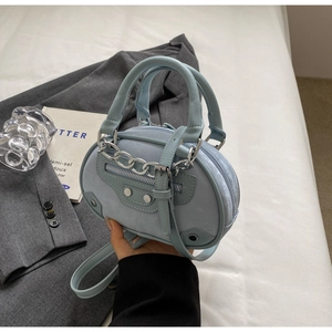 Detail of light blue crossbody bag with silver chains and rivets on grey blazer