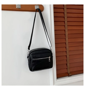 Detalle de bolso bandolera de cuero granulado negro con cremalleras dobles plateadas en percha