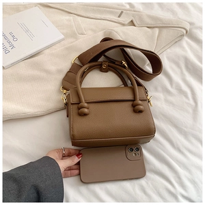 Détail de la texture cuir grainé marron sur un sac à main avec bandoulière large