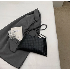 Detail der schwarzen gewebten Kettenumhängetasche auf grauem Blazer im minimalistischen Stil