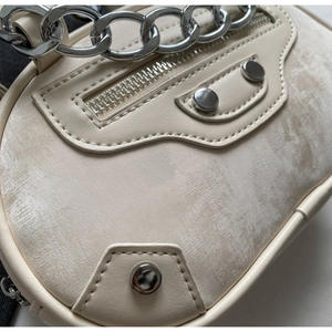 Detail of cream motorcycle bag featuring distressed leather texture and silver chain