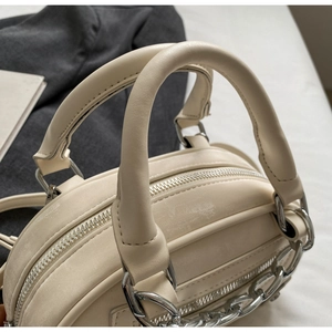 Detail view of cream handbag with silver zippers and elegant decorative chain links