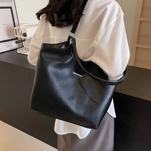Minimalist black pebble leather tote bag with silver metal bar detail on a model