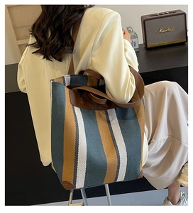 Detail of striped canvas tote bag featuring leather handles and wide shoulder strap
