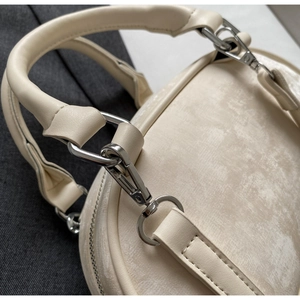Detail of silver metal hardware and smooth leather handle on a cream crossbody bag