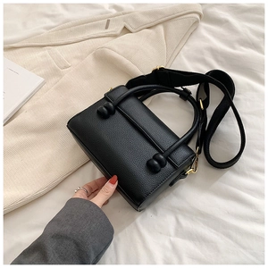 Détail d'un sac à main noir en cuir grainé avec finitions dorées et large bandoulière
