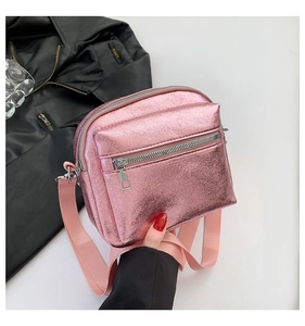 Detalle de bolso bandolera rosa metalizado con cuero sintético texturizado y cremalleras plata