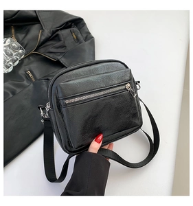 Detalle de bolso bandolera negro con doble cremallera y correa ancha de nailon
