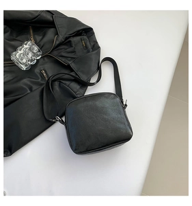 Detalle de bolso bandolera de cuero negro con correa ajustable y cierres de metal plateado