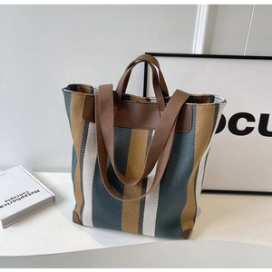 Detail of striped canvas tote bag showing brown leather handles and woven shoulder strap