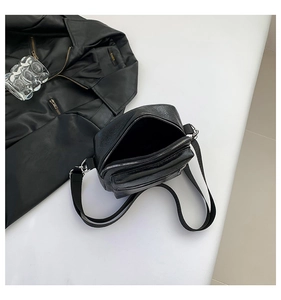 Detalle de un bolso bandolera de cuero negro con doble cremallera y correa ancha