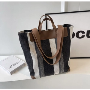 Detail of striped canvas tote bag showing brown leather handles and textured weaving