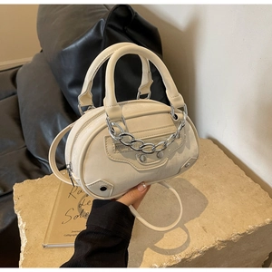 Detail view of cream leather oval bag with silver studs and chain on stone base