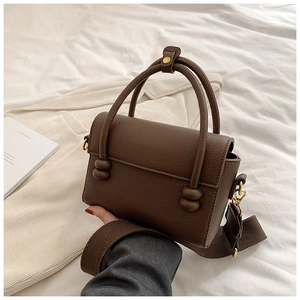 Gros plan du sac à main marron en cuir grainé avec bandoulière large et boucles dorées