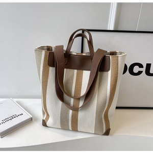Detail view of woven striped canvas tote bag with brown leather reinforcement and handles