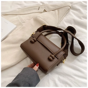 Détail du sac à main marron foncé en cuir litchi avec boucle dorée et bandoulière
