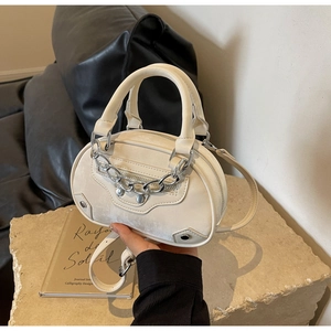 Detail shot of a cream round crossbody bag featuring motorcycle rivets and chain details