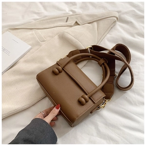 Détail d'un sac à main carré en cuir marron avec bandoulière large et décoration sphérique