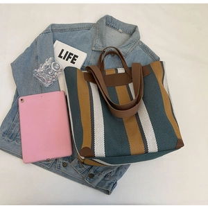 Flat lay of striped canvas tote bag with leather details alongside lifestyle accessories