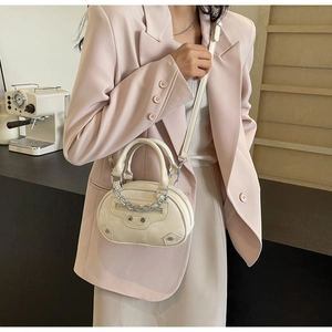 Detail of cream mini oval bag featuring silver studs, decorative zippers and metal chain