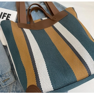 Detail of striped canvas tote bag with brown leather handles on denim background
