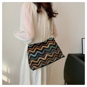 Détail d'un sac seau bohème tissé aux motifs ondulés colorés sur une robe blanche
