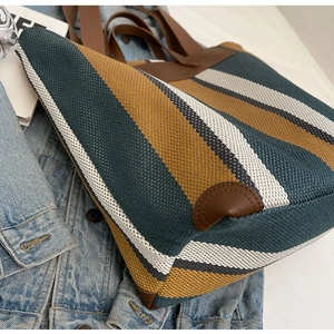 Detail of multi-color striped canvas tote bag with brown leather trim and knit texture