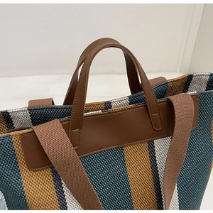 Detail of multi-color striped woven tote bag with leather handle and wide shoulder strap