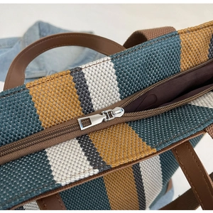 Detail of multi-color striped canvas tote bag with zipper closure and brown handles