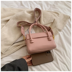 Sac rose texture litchi avec détails dorés et bandoulière large à côté d'un smartphone