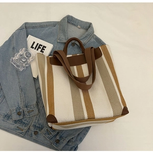 Detail view of striped canvas tote bag with reinforced brown leather handles and base