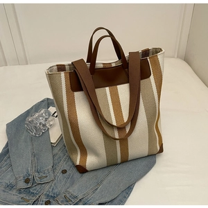 Detail of striped canvas tote bag with brown leather handles on a casual lifestyle background